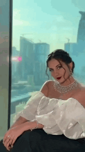 the woman is wearing a white off the shoulder top and a necklace .