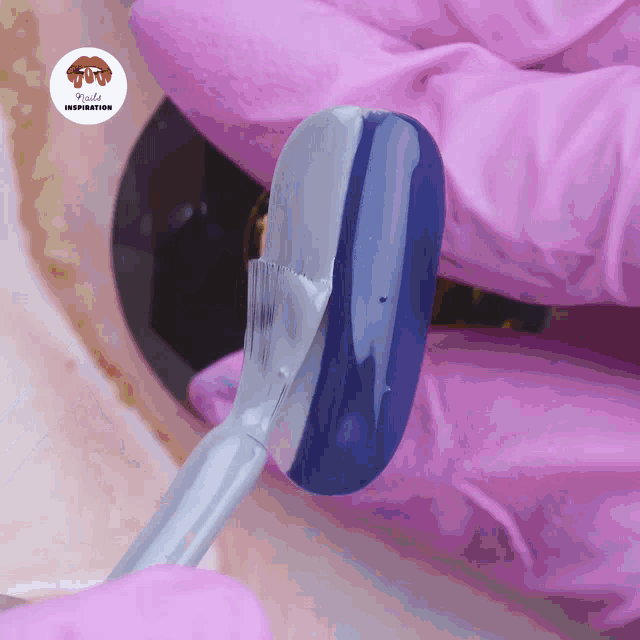 a pink glove is holding a brush and a blue nail polish