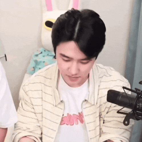 a young man is sitting in front of a microphone wearing a striped shirt with the word sun on it .
