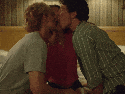 two men and a woman kissing on a bed in a bedroom