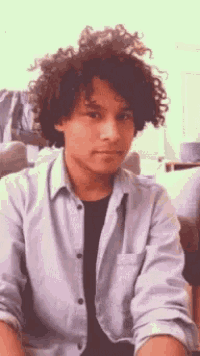 a young man with curly hair is wearing a blue shirt and black shirt