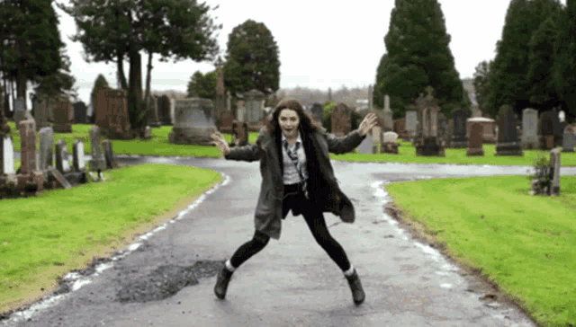 a woman is jumping in the air in a cemetery with her arms outstretched