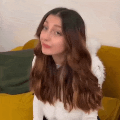 a young woman with long brown hair is sitting on a yellow couch making a funny face .
