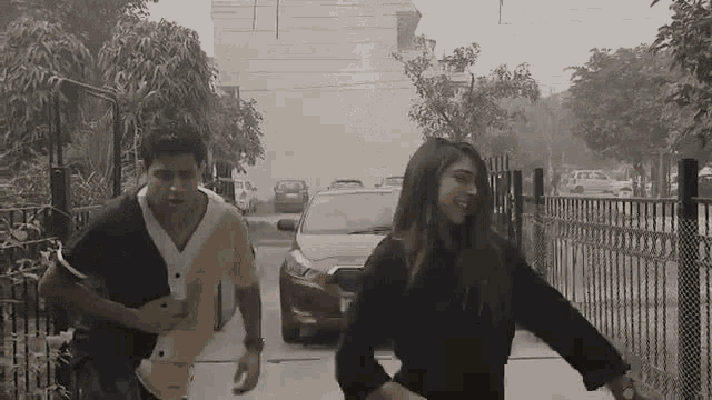 a man and a woman are running down a street in front of a car .
