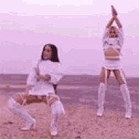 two women in white outfits are dancing on a beach .