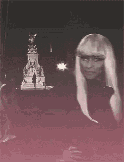 a woman with blonde hair is standing in front of a statue at night .