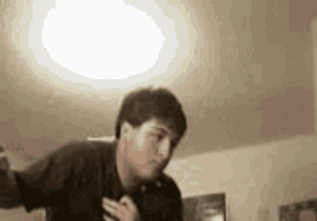 a man in a black shirt is dancing in a room with a light on the ceiling .
