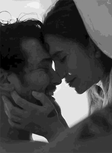 a black and white photo of a man and a woman kissing .