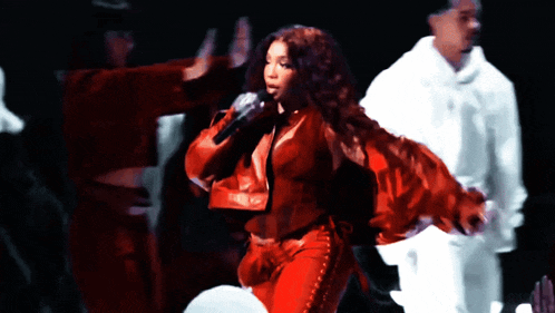 a woman in a red jacket is singing into a microphone on stage
