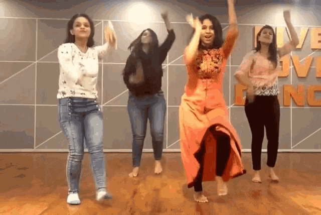 four women are dancing in front of a wall that says love