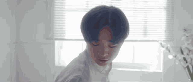 a young man is standing in front of a window with blinds .
