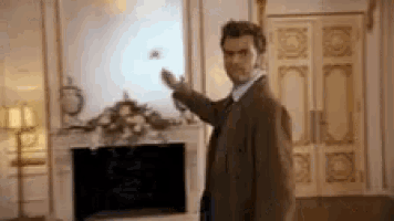 a man in a suit and tie is standing in a living room in front of a fireplace .