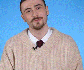 a man with a beard wearing a tan sweater and tie