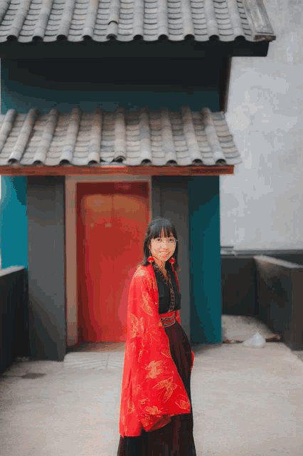a woman in a red dress is standing in front of a building
