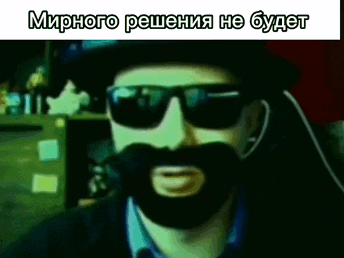 a man with a beard wearing sunglasses and a hat says " мирного решения не будет " in russian