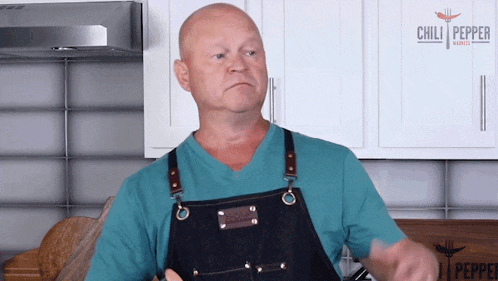 a man wearing an apron in a kitchen with a chili pepper logo in the background