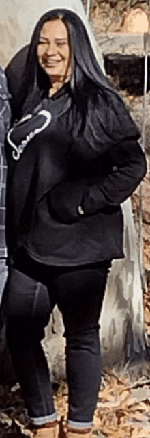 a woman in a black sweatshirt and black pants is smiling while standing next to a man .