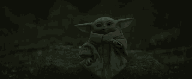 a baby yoda is sitting on top of a mossy rock in the dark .