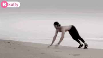 a man without a shirt is doing push ups on a beach .