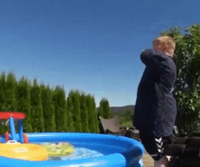 a boy is standing in front of an inflatable pool with a boat in it .
