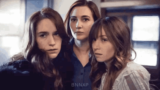 a group of three women are standing next to each other and looking at the camera with a serious look on their faces .