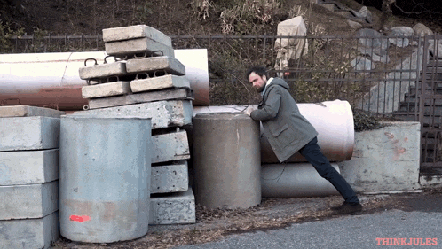 a man is pushing a concrete cylinder in front of a pile of concrete blocks with think jules written on the bottom