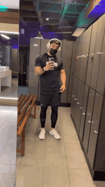 a man wearing headphones and a mask takes a picture of himself in a gym locker room