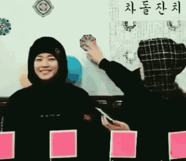a man in a hooded jacket is smiling while another man writes on a white board .