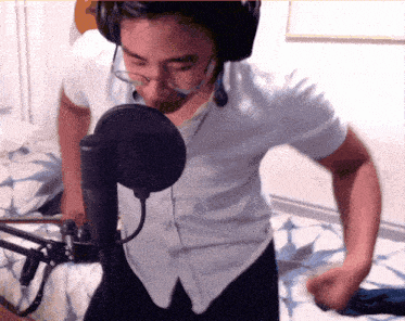 a man wearing glasses and headphones stands in front of a microphone