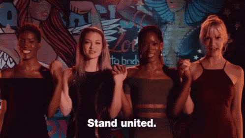 a group of women are holding their fists up in front of a wall that says " stand united " on it