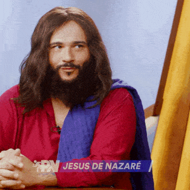 a man with long hair and a beard is wearing a red shirt and a blue scarf with jesus de nazare written on it