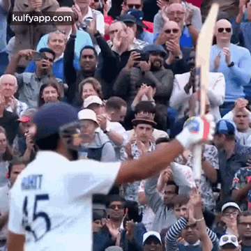 a cricket player is holding up his bat in front of a crowd of people .
