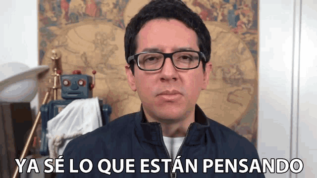 a man with glasses says ya se lo que estan pensando in front of a robot