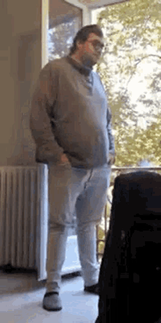 a man is standing in front of a window wearing sunglasses and a sweater .