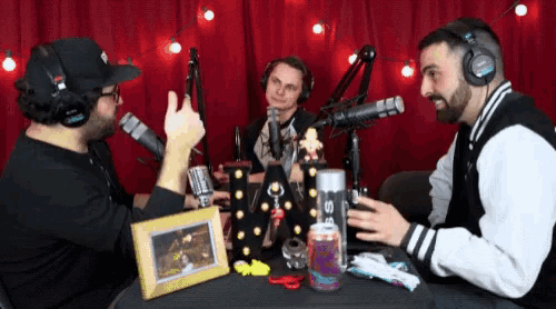 a man wearing headphones talks into a microphone while two other men look on