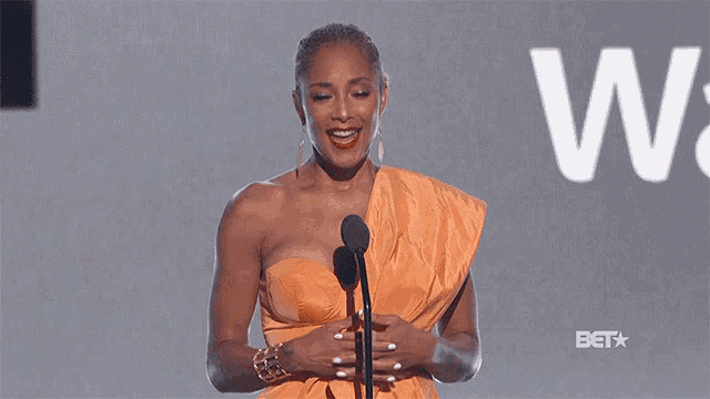 a woman in an orange dress is standing in front of a microphone and smiling ..