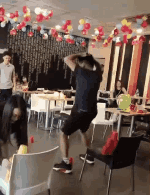 a man is standing on a chair in a restaurant with balloons hanging from the ceiling