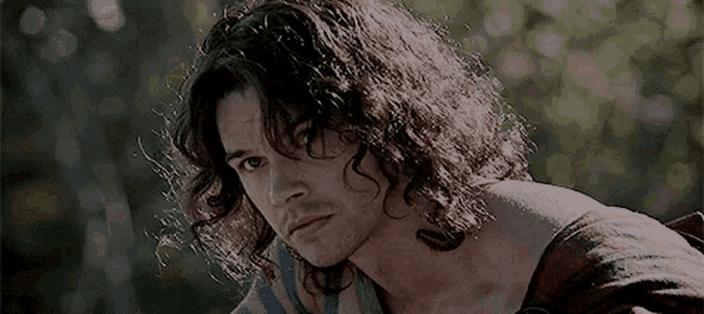 a man with long hair and a tattoo on his arm is looking at the camera .
