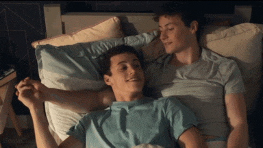 two young men are laying in a bed holding hands .