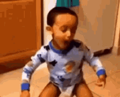 a little boy is sitting on the floor in a kitchen wearing a blue shirt .