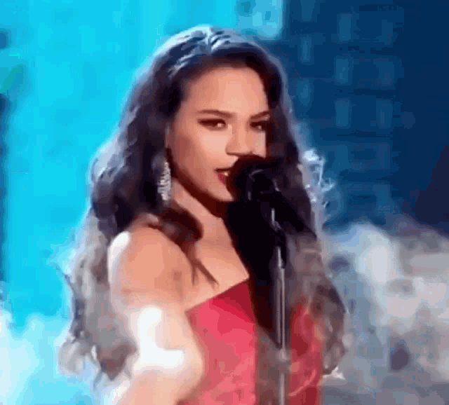 a woman in a red dress is singing into a microphone on stage .