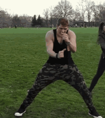 a man in a black tank top and camouflage pants is dancing in a field