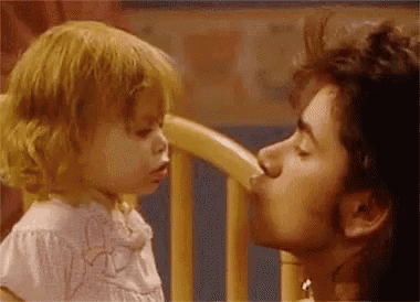a man is kissing a little girl on the cheek in a chair .