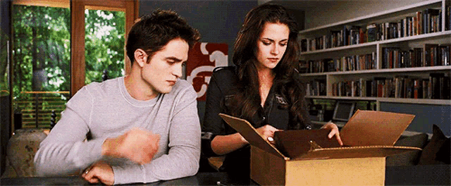 a man and a woman sitting at a table looking at a box .