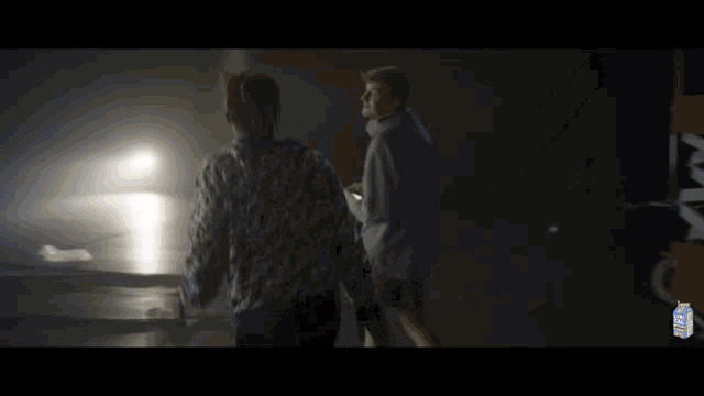 two men are standing next to each other in a dark room in a video .