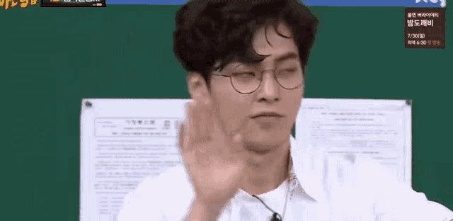 a man with glasses is waving his hand in front of a green board .