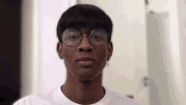 a young man wearing glasses and earrings is making a funny face .