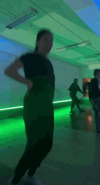 a woman in a black shirt is dancing in a dark room with green lights