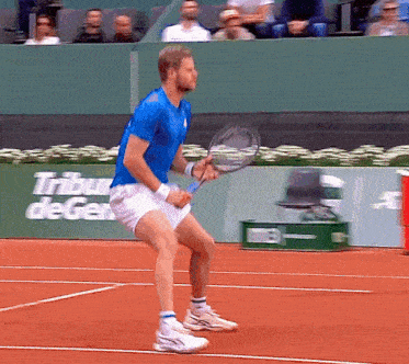 a man in a blue shirt is holding a tennis racquet on a tennis court in front of a tribune de ger
