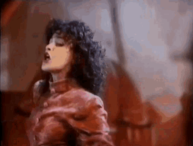 a woman with curly hair and a red jacket is dancing in a dark room .